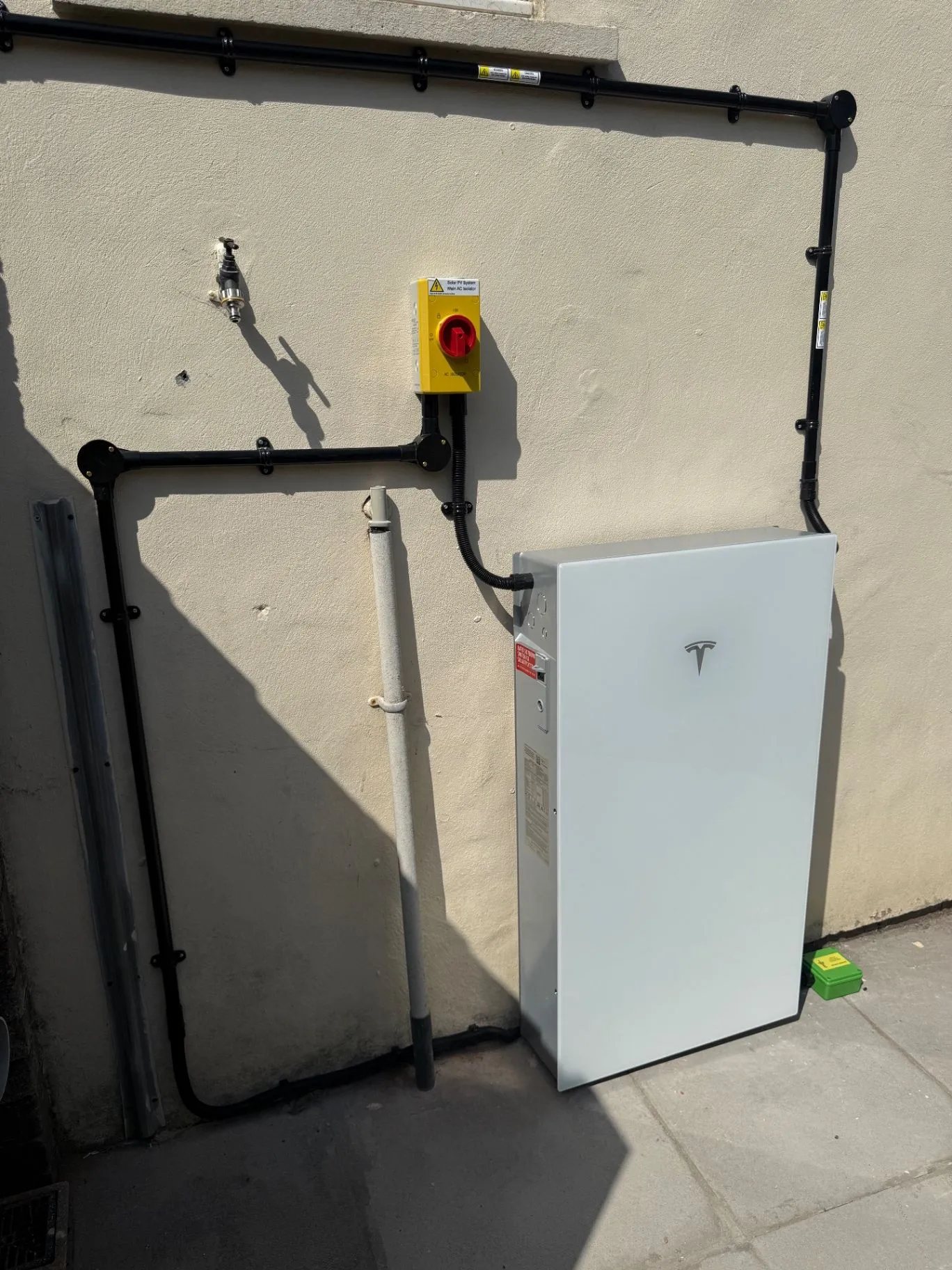 White battery storage unit and red isolator mounted on an exterior wall