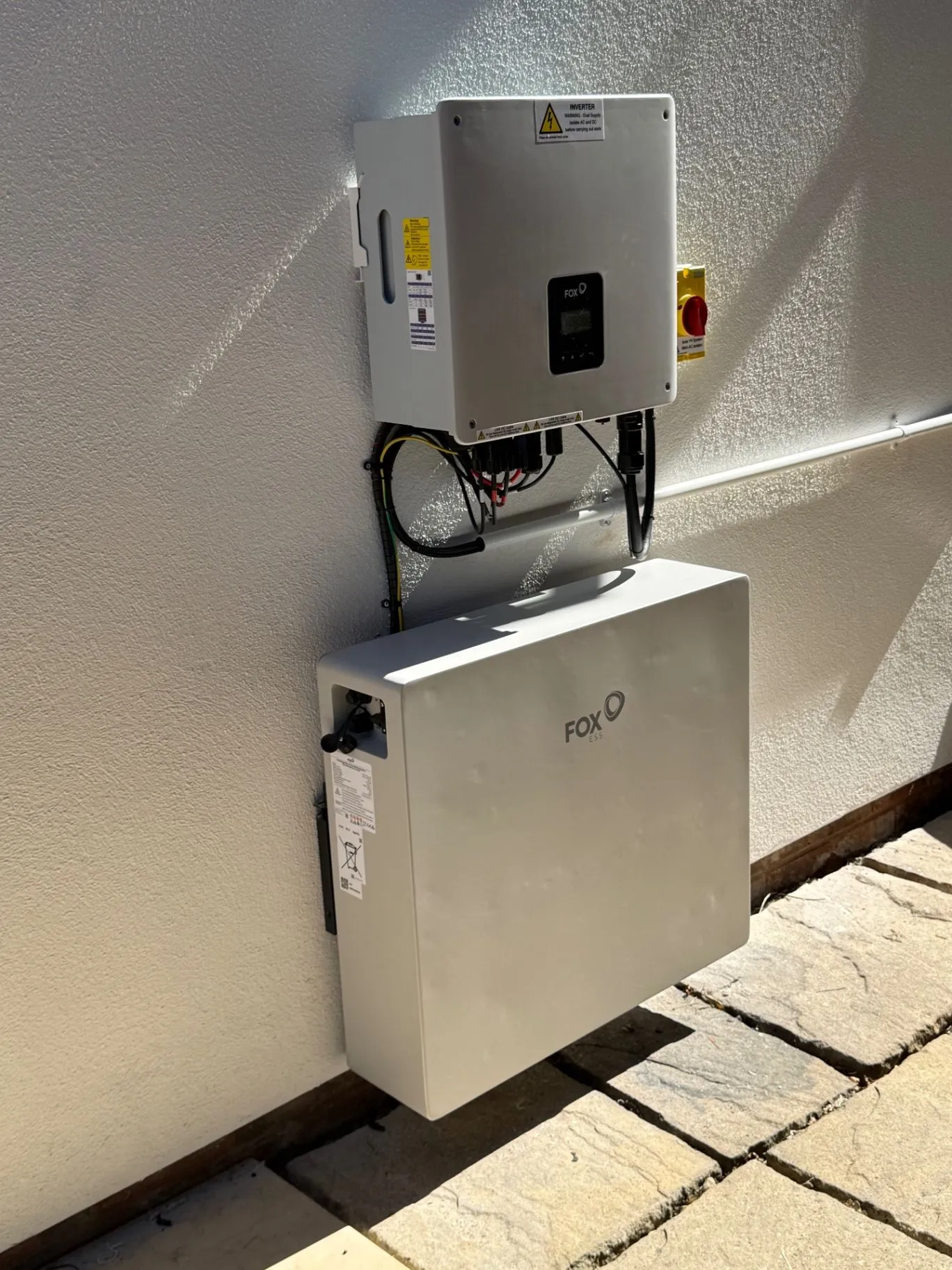 Wall-mounted inverter above a white battery storage unit with visible cabling
