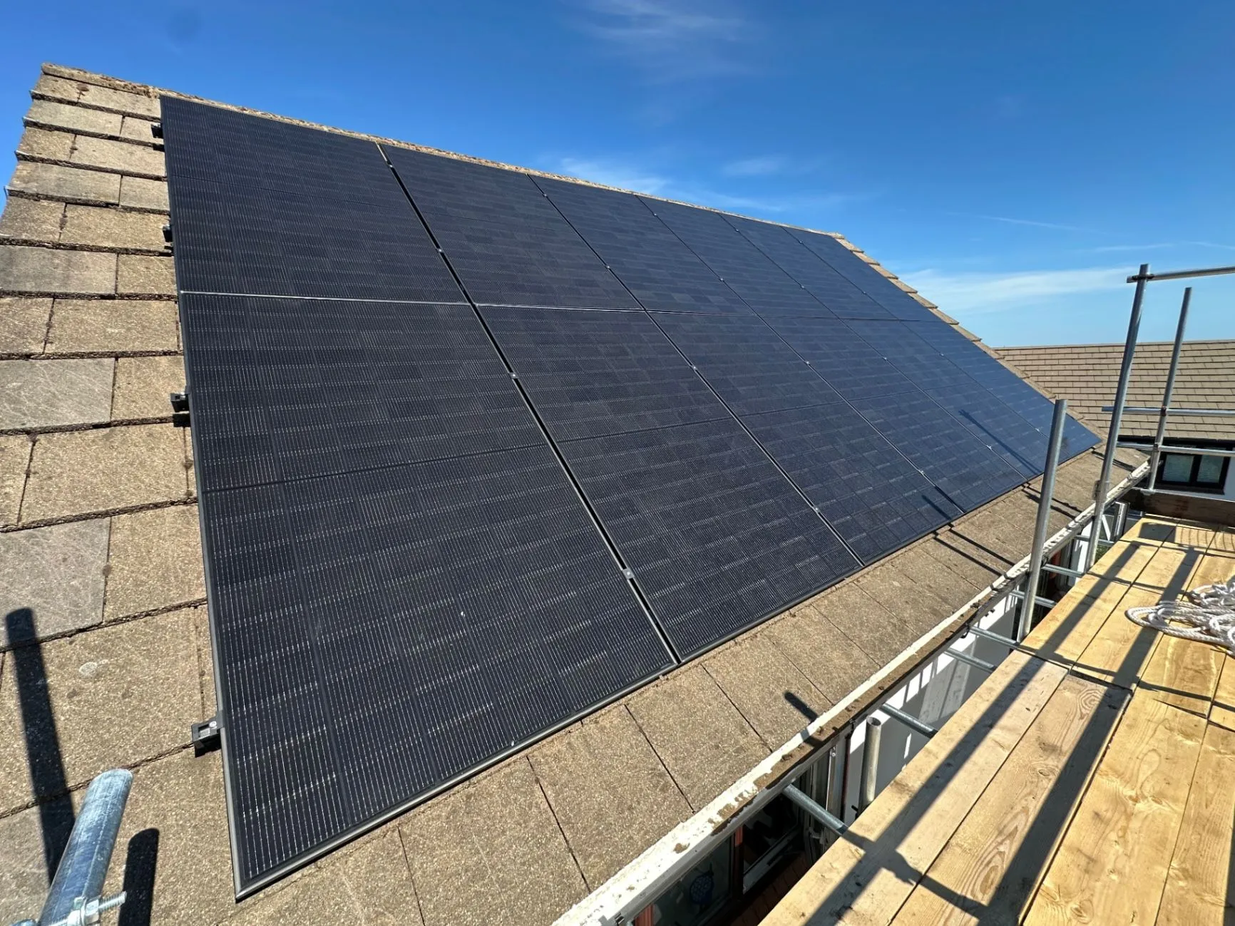 Rows of dark solar panels installed on a pitched roof beside scaffolding
