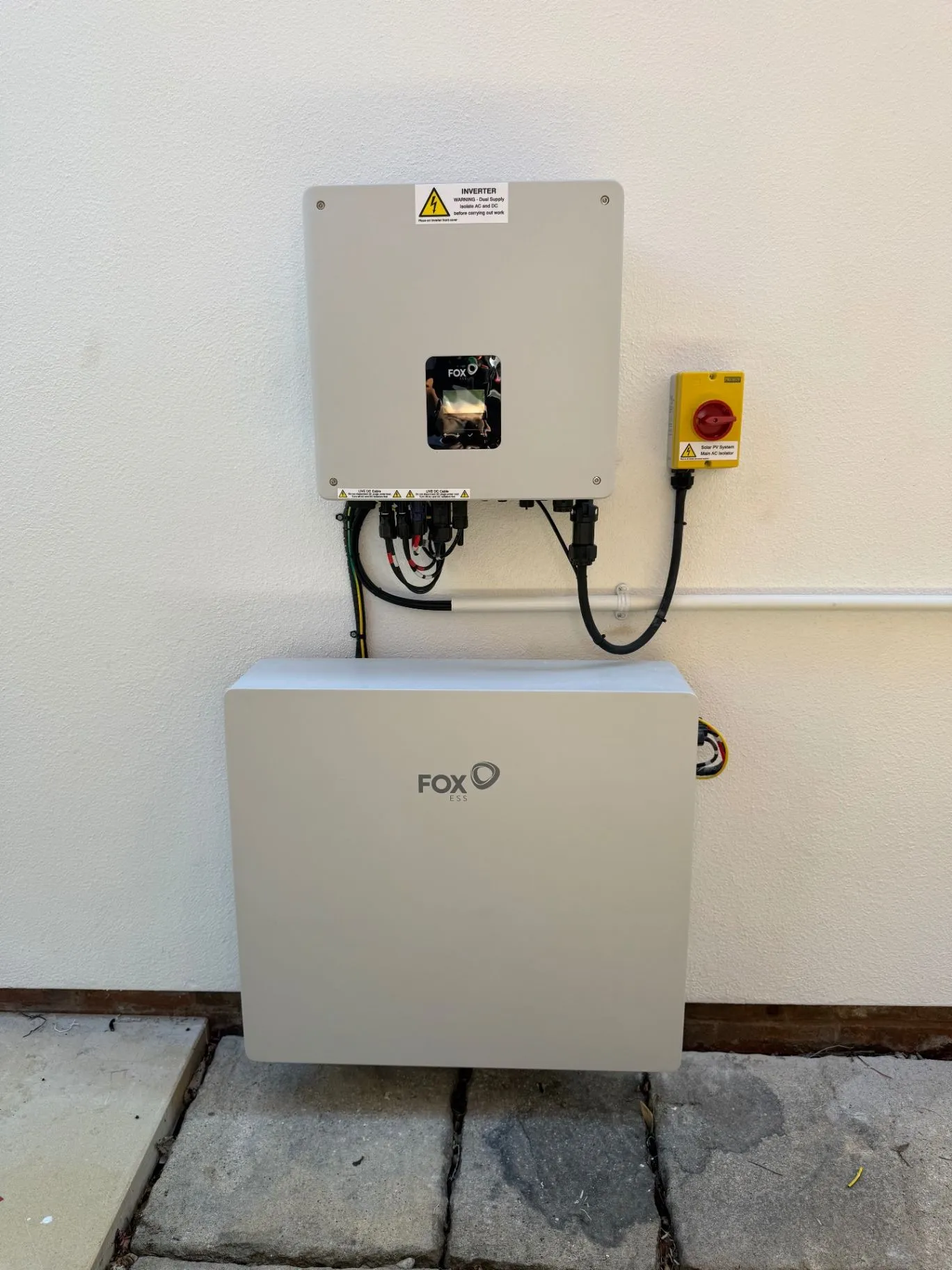 Wall-mounted inverter above a white battery storage unit beside a red isolator