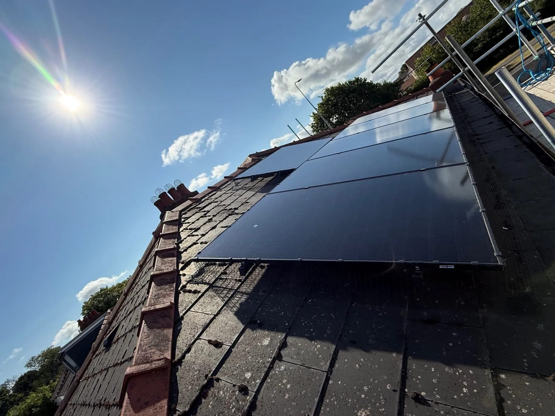 Dark solar panels installed on a pitched roof under a bright blue sky
